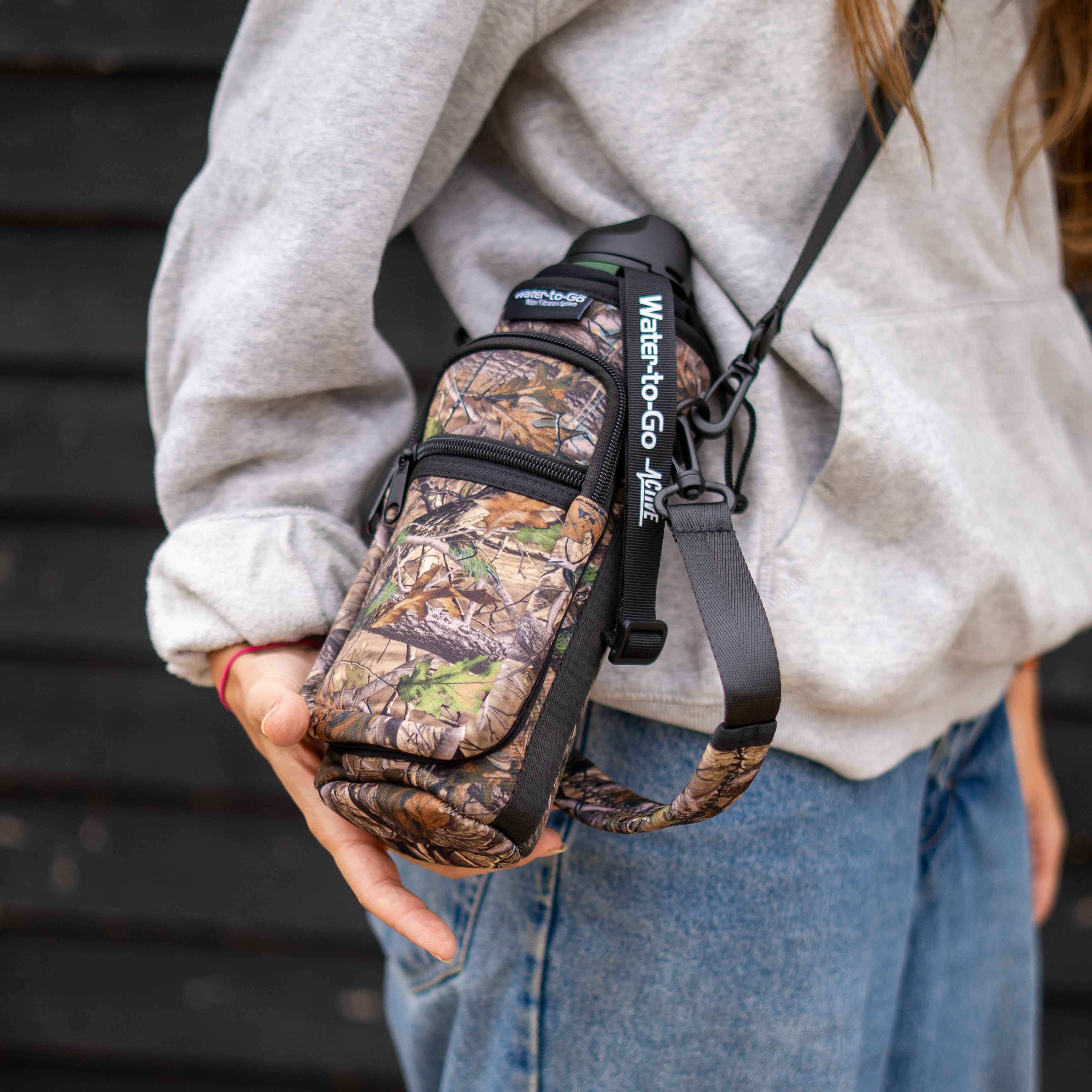 young lady wearing a water to go Insulated Bottle Carrier in camo colourway
